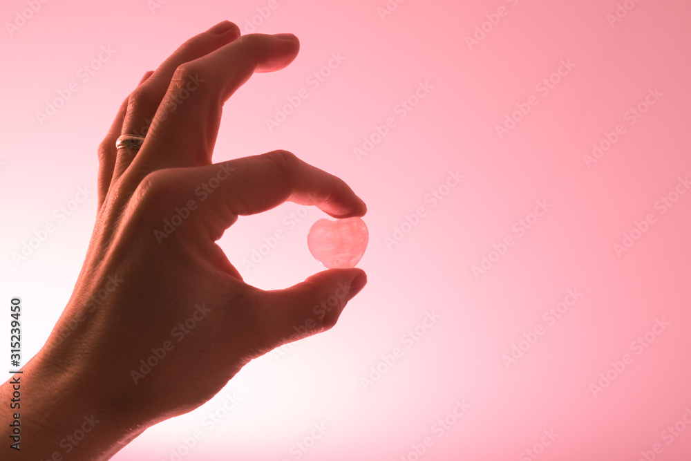 Closeup of hand holding a small heart between two fingers Closeup of hand holding a small heart between two fingers