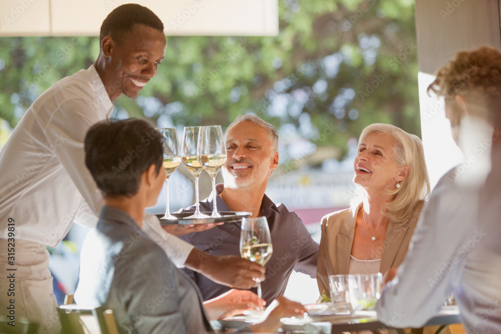 Waiter serving white wine to couples at restaurant table Waiter serving white wine to couples at restaurant table
