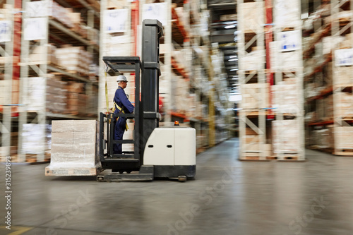 Worker operating forklift moving pallet of boxes in distribution warehouse