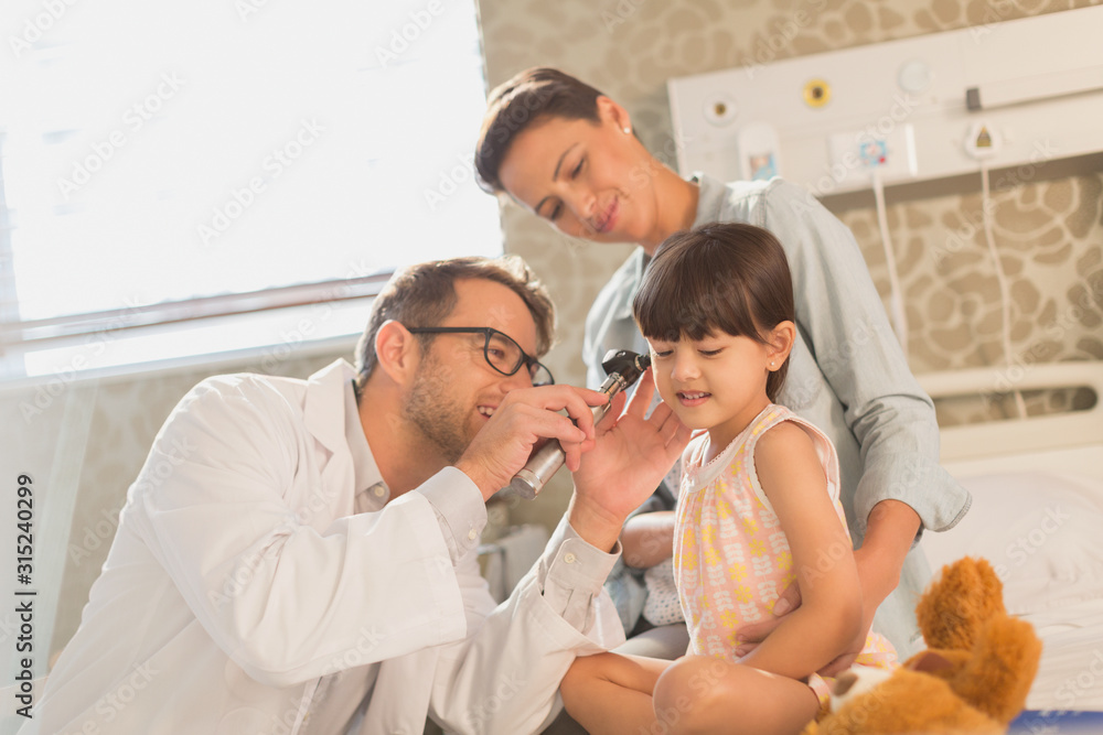 Male doctor using otoscope in ear of girl patient in hospital room Male doctor using otoscope in ear of girl patient in hospital room