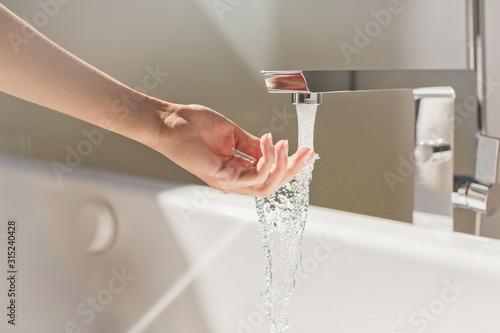 Woman touching water from modern bathtub faucet