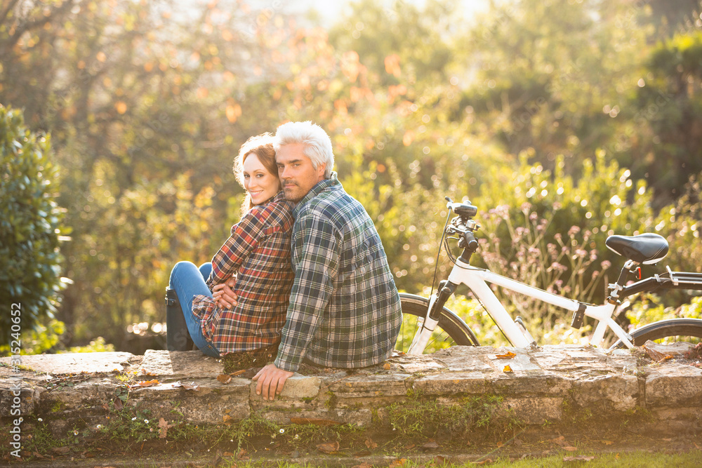© Justin Pumfrey/Caia Image - Portrait affectionate couple with bicycle resting on stone wall in autumn park