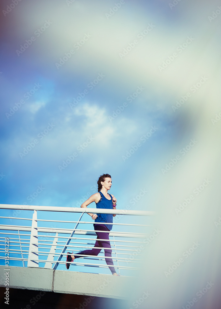 Female runner running on sunny footbridge Female runner running on sunny footbridge
