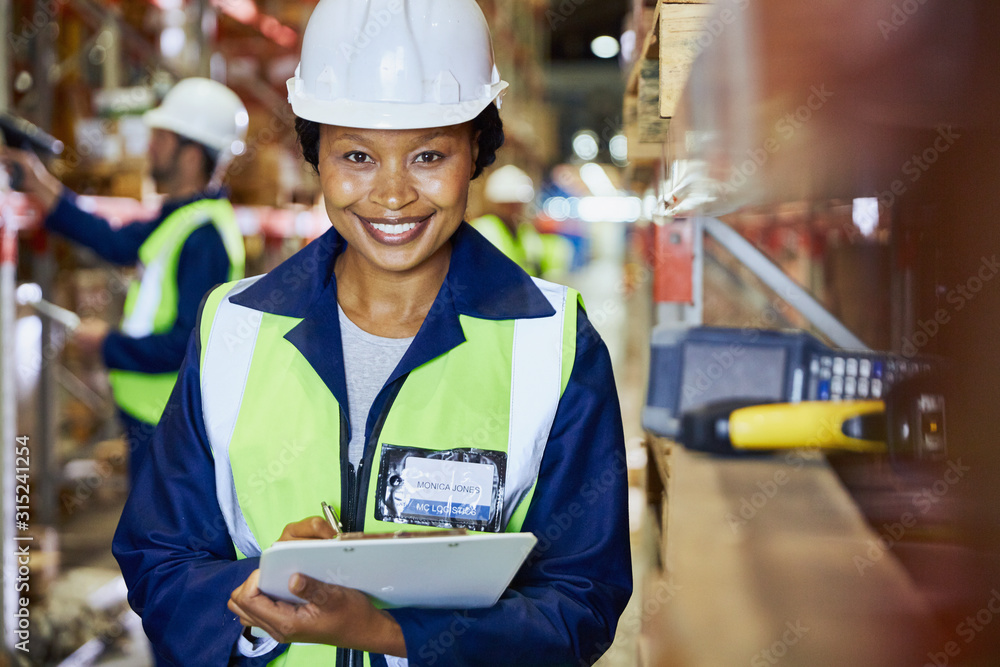 Portrait smiling female worker with clipboard in distribution warehouse Portrait smiling female worker with clipboard in distribution warehouse