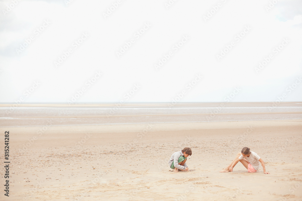 Brother and sister playing in sand on overcast summer beach Brother and sister playing in sand on overcast summer beach