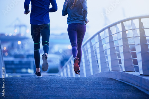 Runner couple running on urban footbridge at dawn