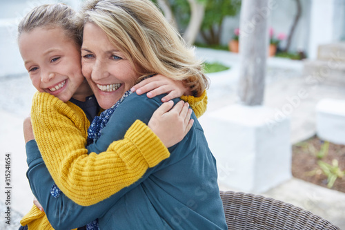 Enthusiastic grandmother and granddaughter hugging on patio
