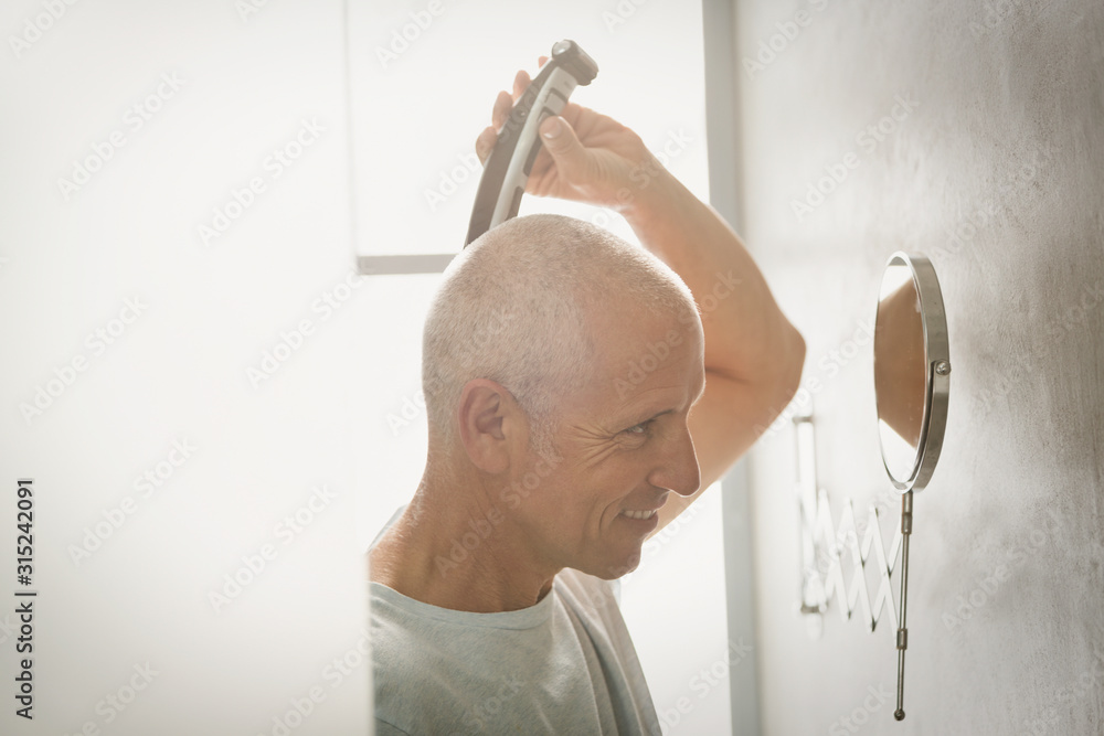Mature man shaving head with electric razor in bathroom Mature man shaving head with electric razor in bathroom
