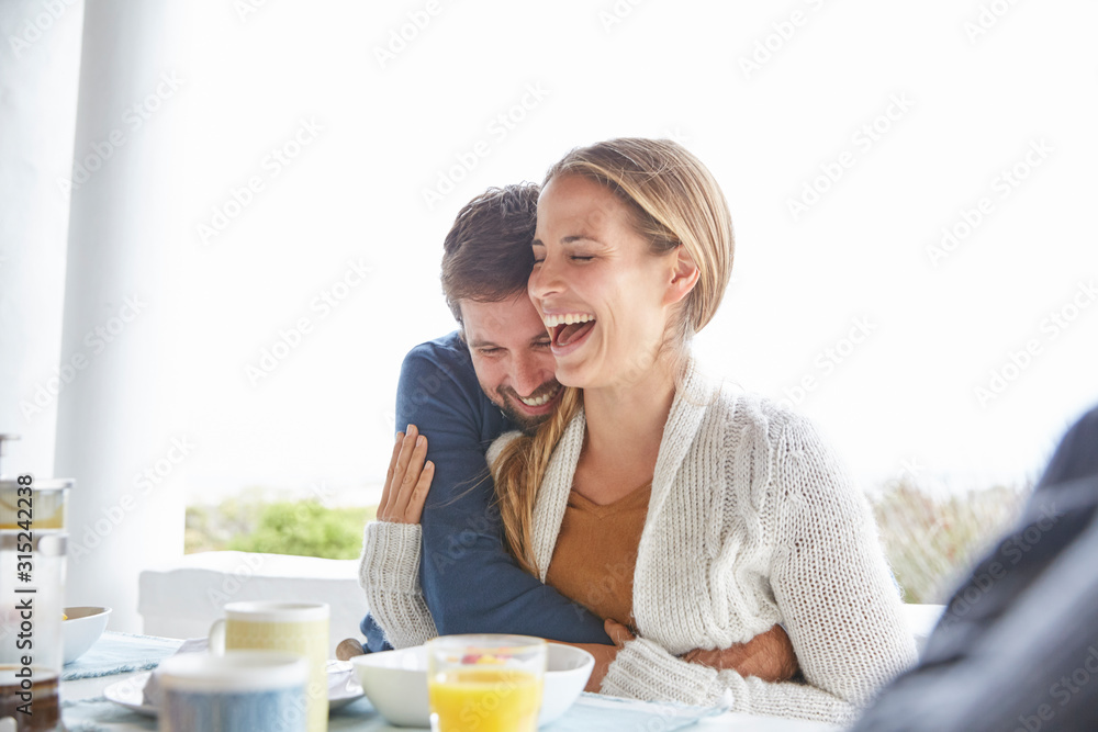 Affectionate couple hugging and laughing at breakfast on patio Affectionate couple hugging and laughing at breakfast on patio