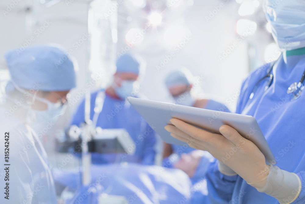 Surgeon wearing rubber gloves, using digital tablet in operating room Surgeon wearing rubber gloves, using digital tablet in operating room