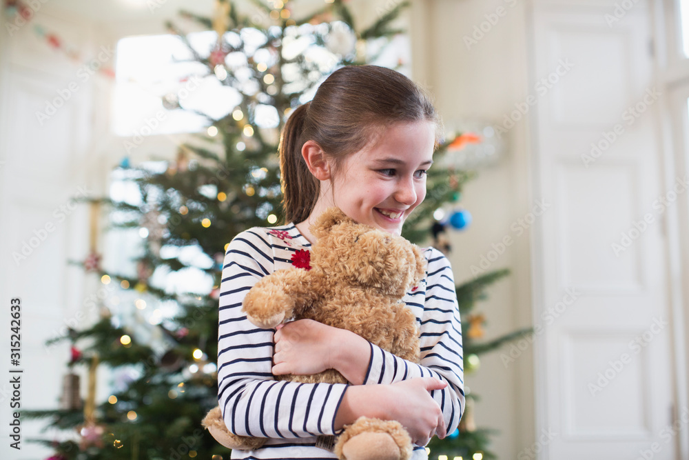 Happy girl hugging teddy bear in front of Christmas tree Happy girl hugging teddy bear in front of Christmas tree