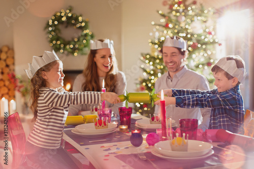 Family in paper crowns pulling Christmas cracker at dining table photo