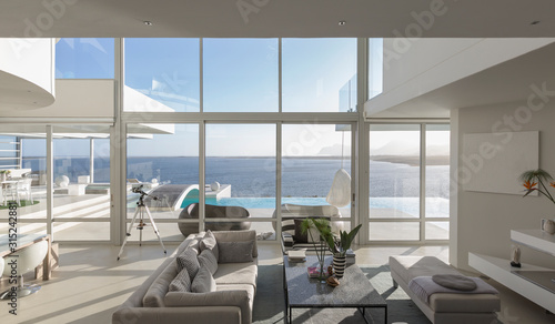 Sunny, tranquil modern luxury home showcase interior living room with patio and ocean view photo