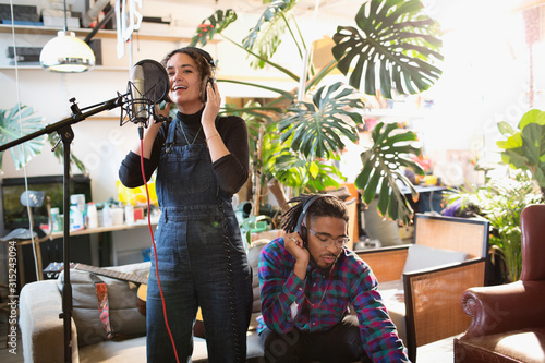 Young man and woman recording music in apartment, singing into microphone