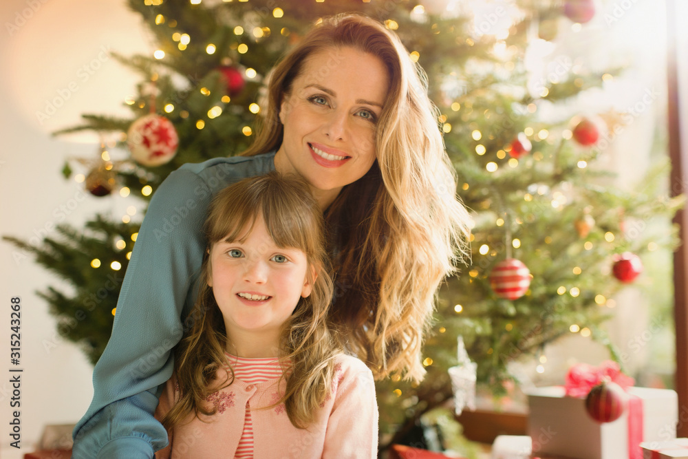 Portrait smiling mother and daughter in front of Christmas tree Portrait smiling mother and daughter in front of Christmas tree