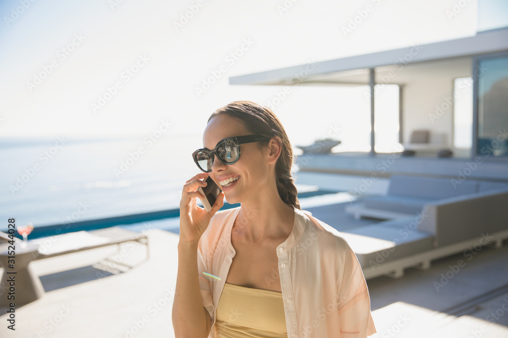 Smiling woman talking on smart phone on sunny modern, luxury home showcase exterior patio Smiling woman talking on smart phone on sunny modern, luxury home showcase exterior patio