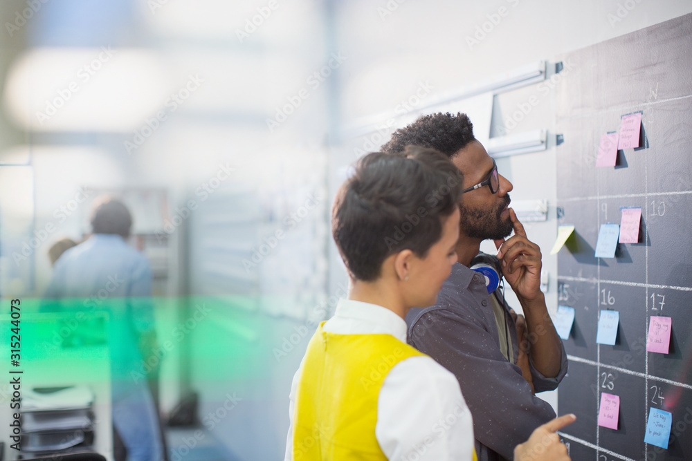 © Tom Merton/Caia Image - Thoughtful, creative business people planning, scheduling at calendar blackboard