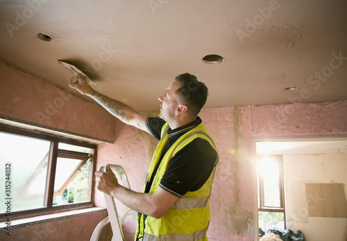 Construction worker plastering ceiling in house