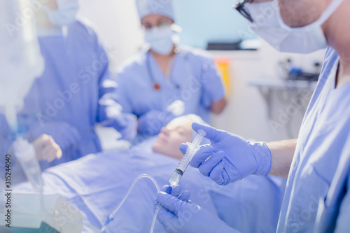 Anesthesiologist with syringe injecting anesthesia into IV drip in operating room photo