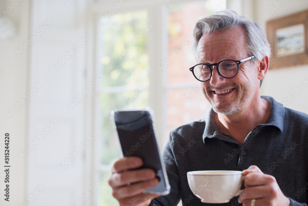Smiling mature man drinking tea and using smart phone Smiling mature man drinking tea and using smart phone