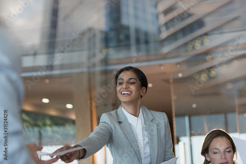 Smiling businesswoman handing paperwork to colleague in conference room meeting photo