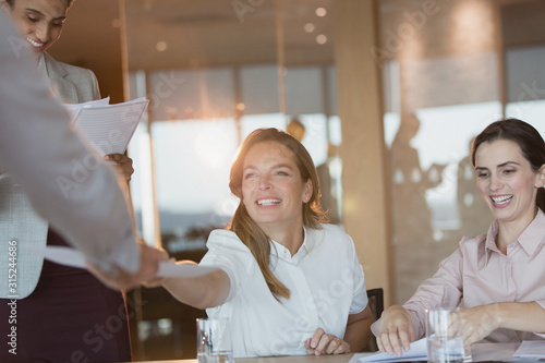 Foto Smiling businesswoman handing paperwork to colleague in conference room meeting