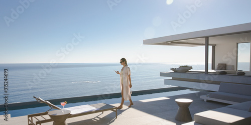 Woman walking on sunny, modern, luxury home showcase exterior patio with ocean view