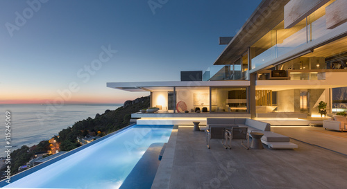 Illuminated modern, luxury home showcase exterior patio with lap pool and ocean view at twilight