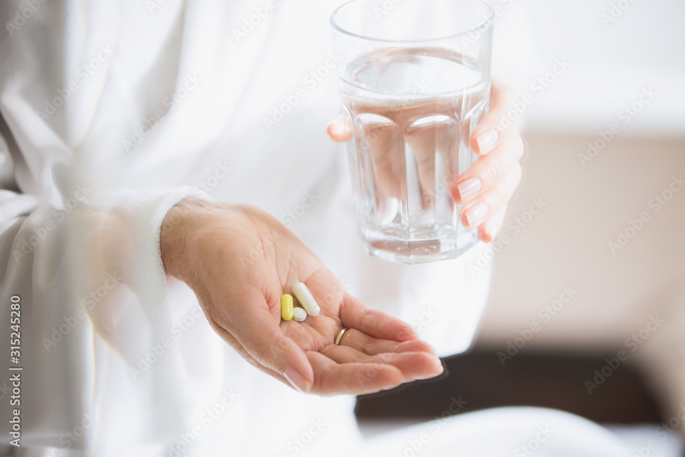 Woman taking vitamins with glass of water Woman taking vitamins with glass of water
