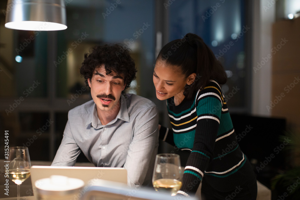 Couple using laptop and drinking white wine at home at night Couple using laptop and drinking white wine at home at night