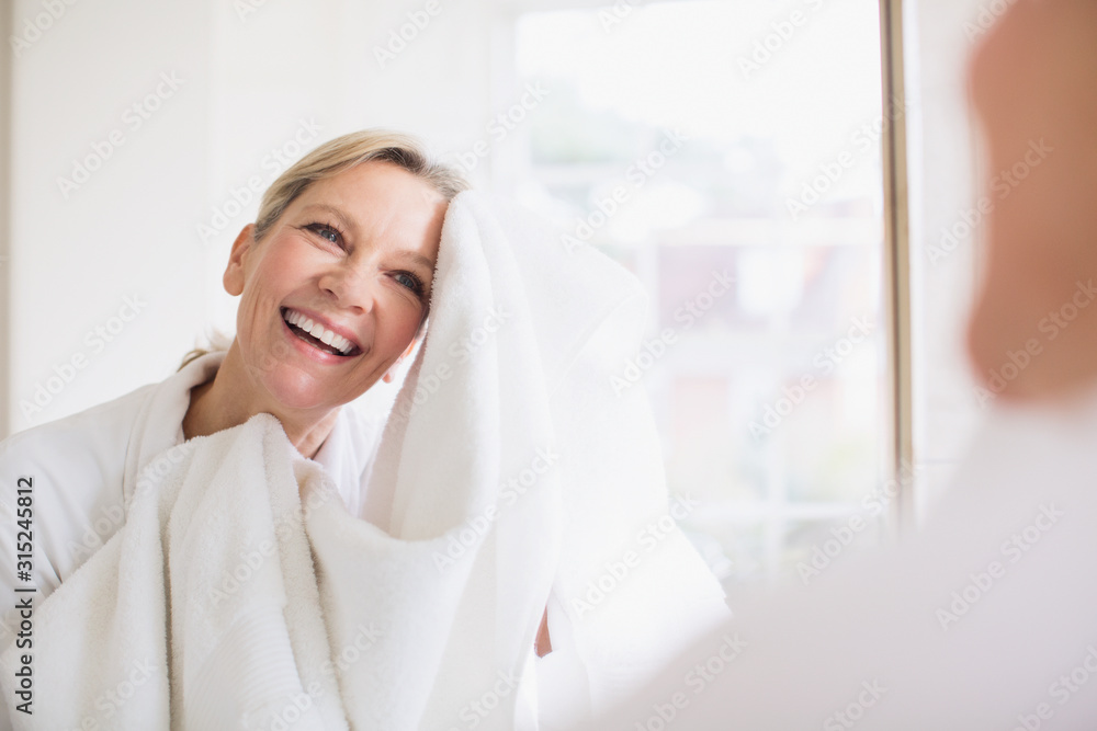 Smiling mature woman drying face with towel at bathroom mirror Stock
