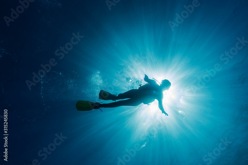 Sun shining behind woman scuba diving underwater, Maldives, Indian Ocean photo