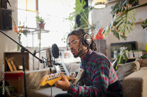 Young male musician recording music, playing guitar at microphone in apartment photo