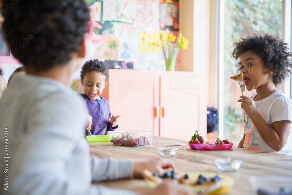 Toddler brother and sister eating breakfast at dining table