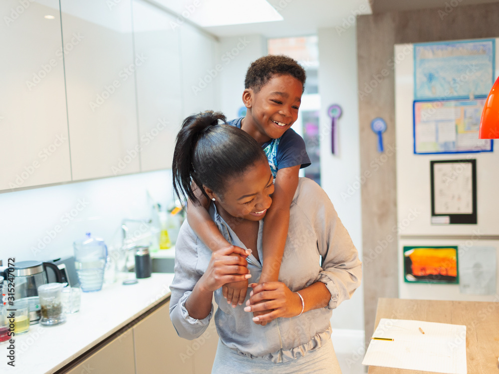 © Paul Bradbury/Caia Image - Playful mother and son piggybacking in kitchen © Paul Bradbury/Caia Image - Playful mother and son piggybacking in kitchen