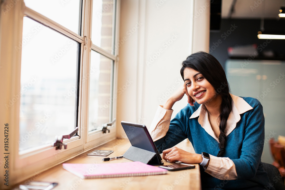 Portrait confident, smiling businesswoman using digital tablet in window Portrait confident, smiling businesswoman using digital tablet in window