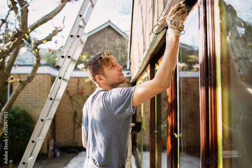 Male painter painting home exterior window trim photo