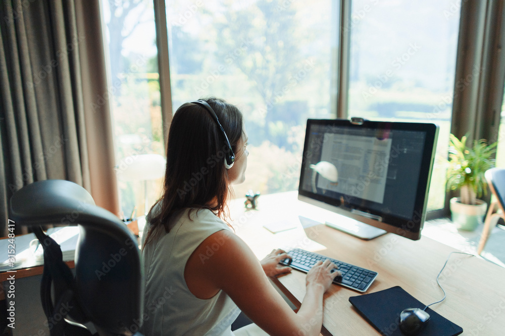 © Paul Bradbury/Caia Image - Businesswoman with headset working at computer in home office