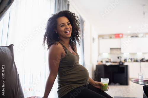Happy young pregnant woman drinking green smoothie