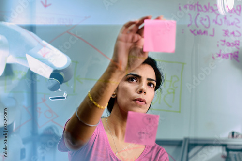 Focused female engineer planning, using adhesive notes in office