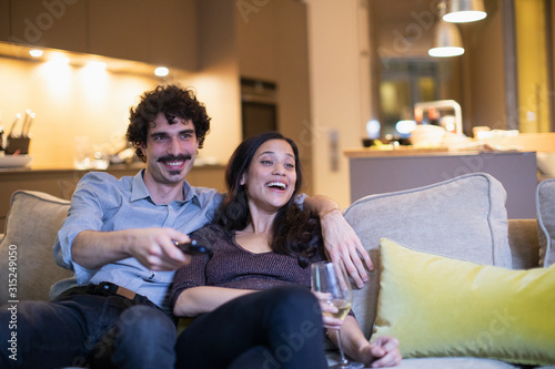 Happy couple watching TV and drinking white wine on living room sofa photo