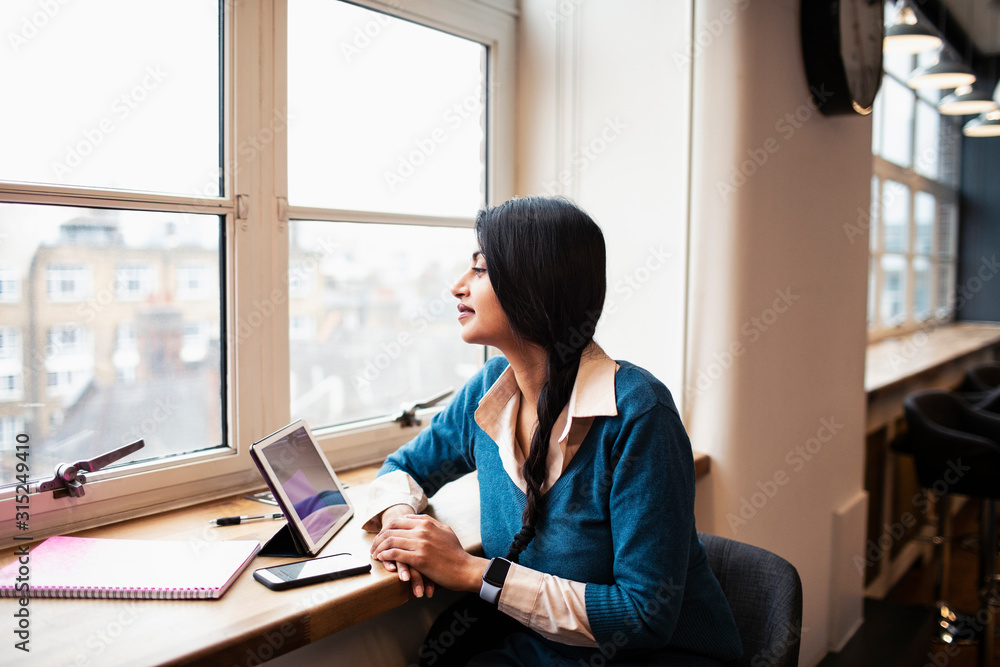 Thoughtful businesswoman working at digital tablet in office window Thoughtful businesswoman working at digital tablet in office window