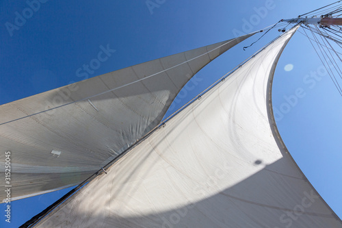 Sailboat sails blowing in breeze below sunny blue sky
