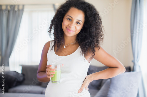 Portrait happy young pregnant woman drinking healthy green smoothie photo