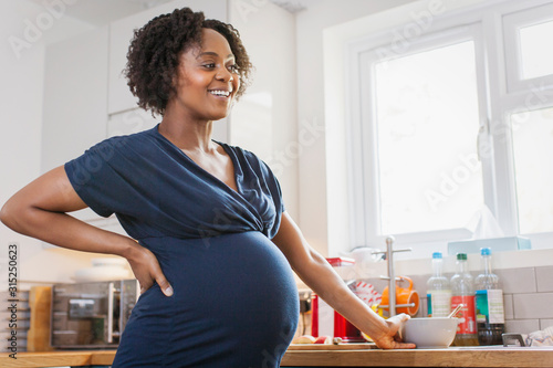 Happy pregnant woman eating in kitchen photo