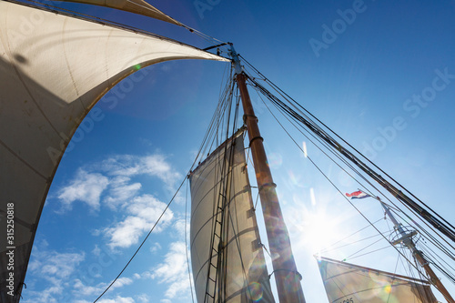 Wooden and mast and sailboat sails below sunny blue sky photo