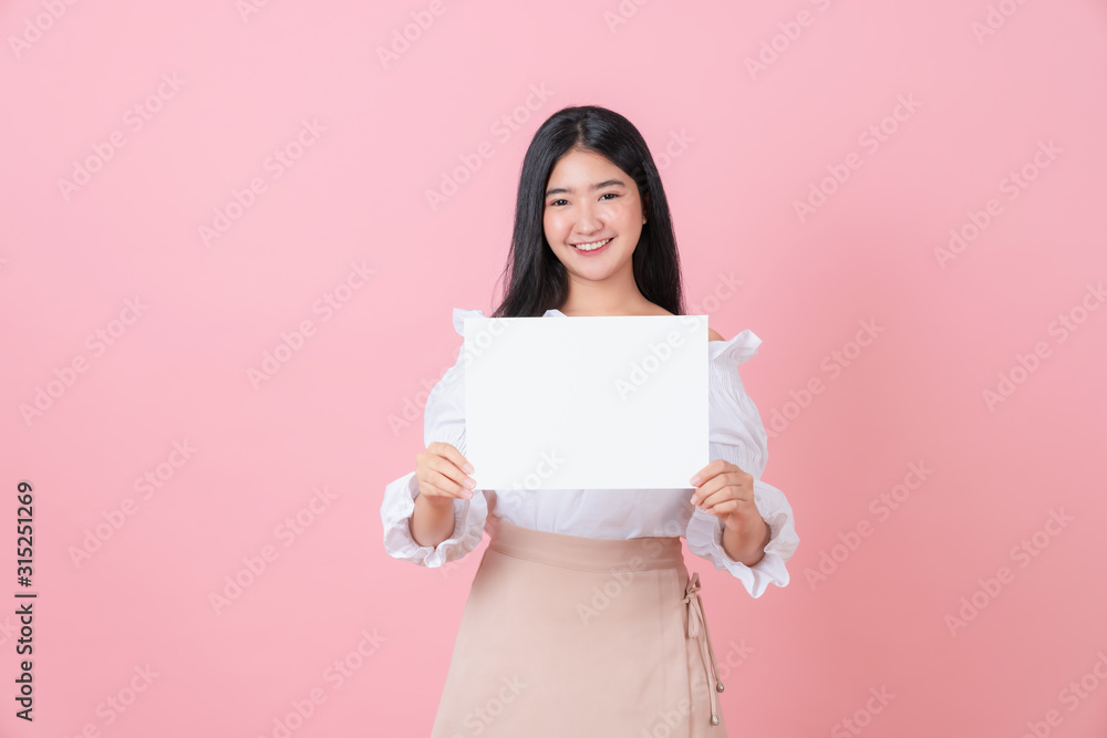 Young Asian woman holding blank paper with smiling face and looking on the pink background. for advertising signs. Young Asian woman holding blank paper with smiling face and looking on the pink background. for advertising signs.
