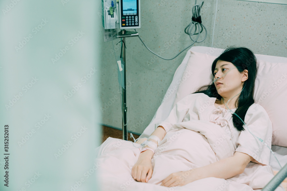 Asian young woman patients lying in hospital room. sick female had severe  aches after car accident. injured lady wearing nasal cannula in bed looking  aside with depressed emotion at night. Stock Photo