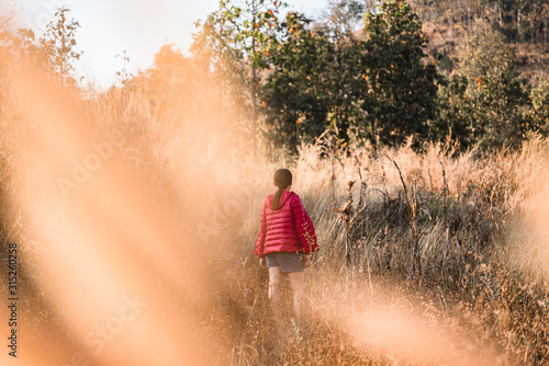 A girl walking on a mountain of brown grass © ณัฐวุฒิ เงินสันเทียะ
