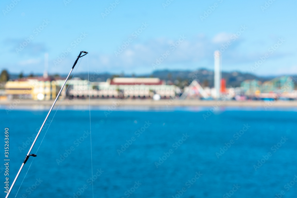 Fishing rod with fishing line. Blurred coastline on horizon under blue sky with clouds